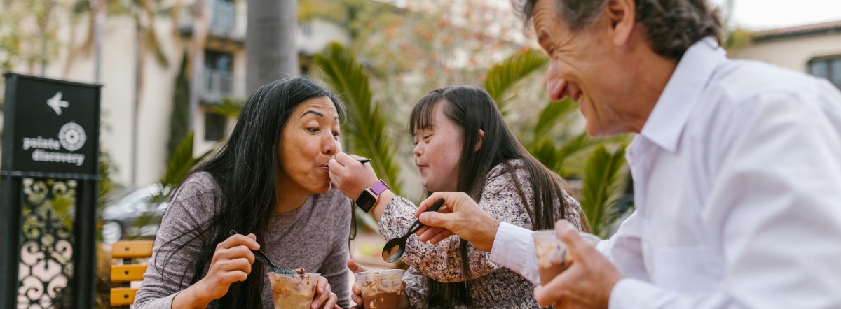 a daughter with down syndrome eats chocolate ice cream outside with her mom and dad