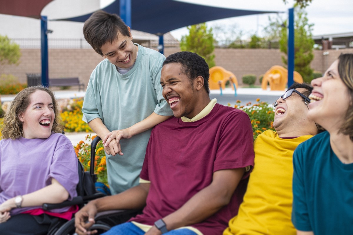 Happy young and diverse adults enjoying each other's company outdoors, many of them with developmental and physical disabilties, sharing laughs and smiles.